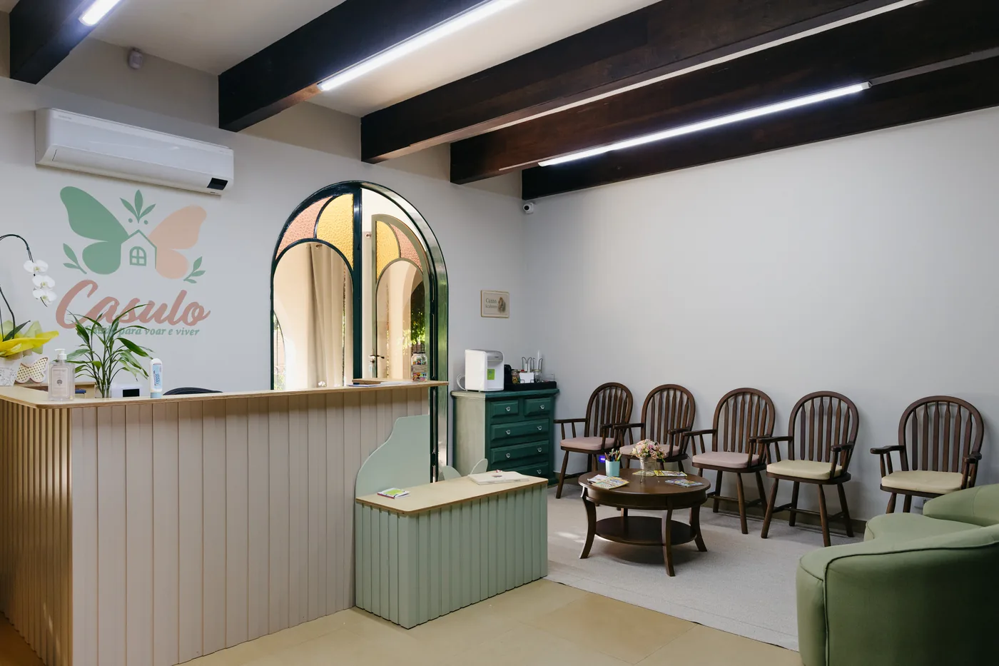 Sala de espera do Espaço Casulo, com cadeiras de madeira, poltrona verde e luz natural